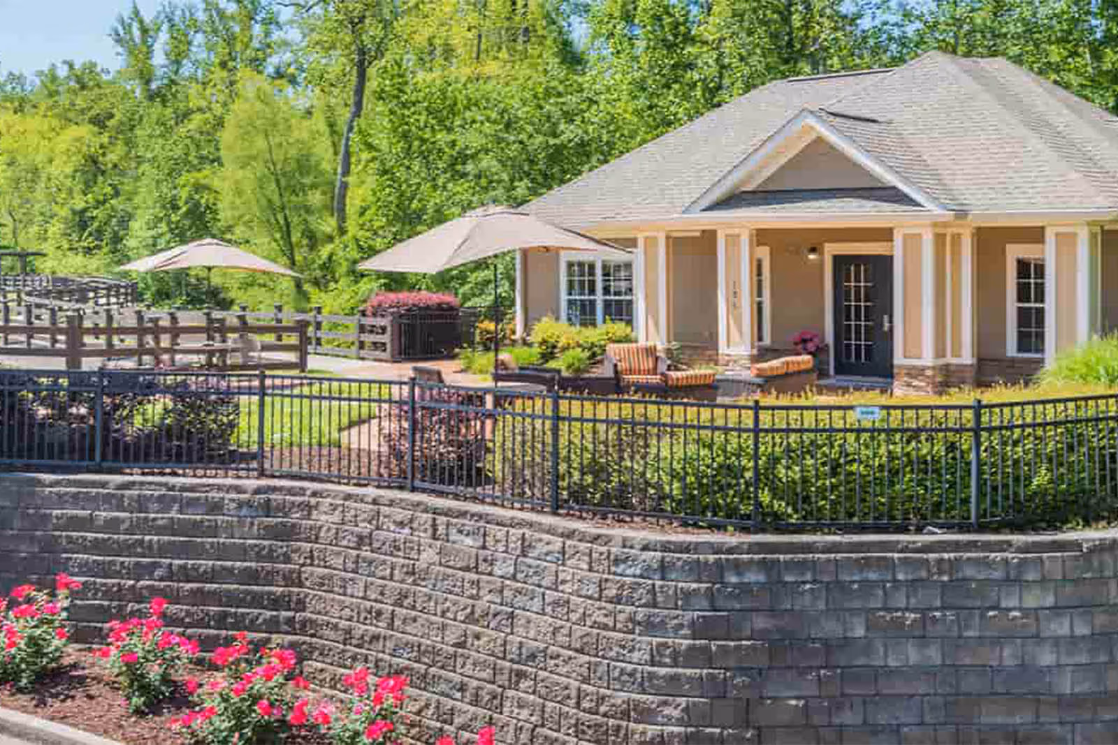 Front exterior of a single-story clubhouse with a patio, umbrellas, seating, and landscaped grounds.