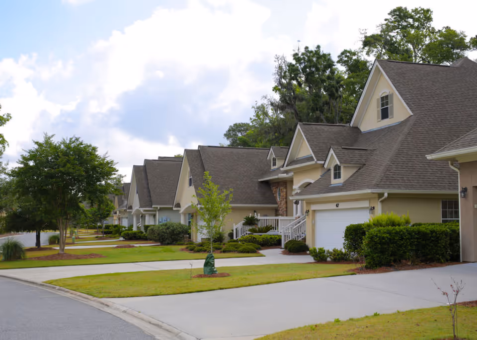 Row of townhouse-style homes with garages, driveways, and landscaped lawns along a suburban street.