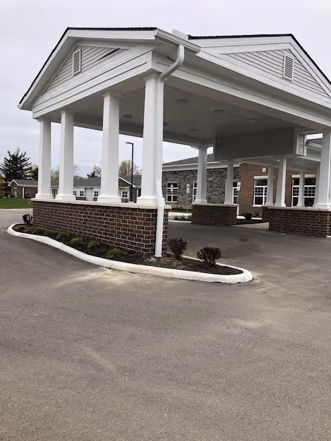 Covered porte-cochere with white columns and brick bases at the front entrance of a care facility.