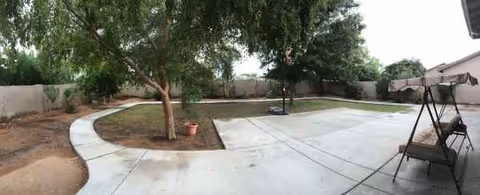 Outdoor courtyard at Caring Hearts Assisted Living: curved concrete path, trees, and a wooden swing bench.