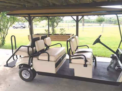 Cream-colored golf-cart with beige seating under a shaded outdoor shelter.