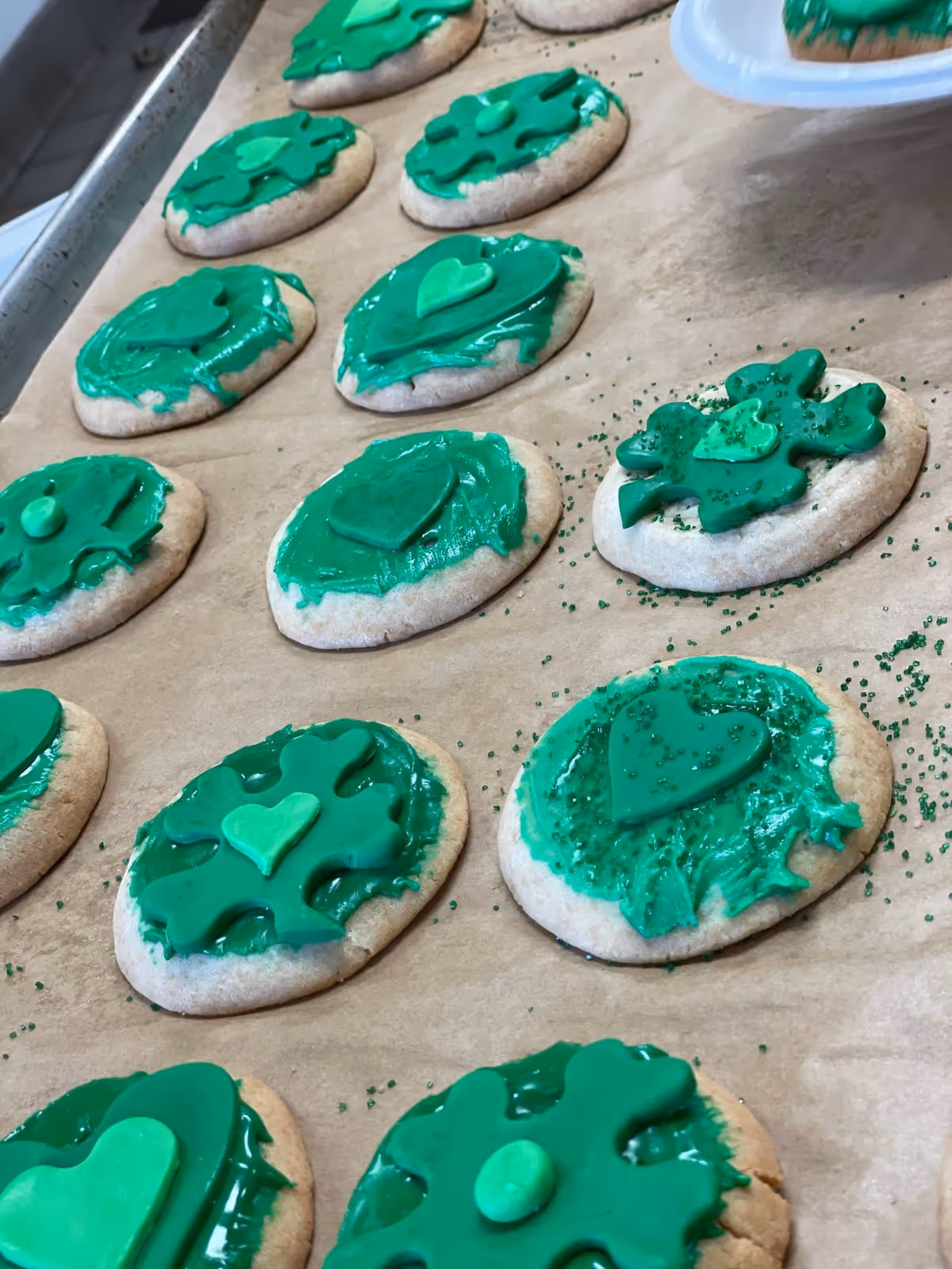 Round sugar cookies on parchment paper decorated with green frosting and shamrock and heart shapes.