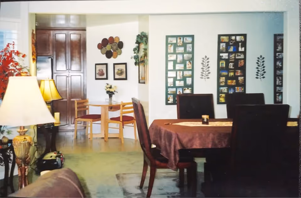 Open-plan dining and sitting area with a round dining table and chairs, a small breakfast nook, wall photo displays, and lamps.