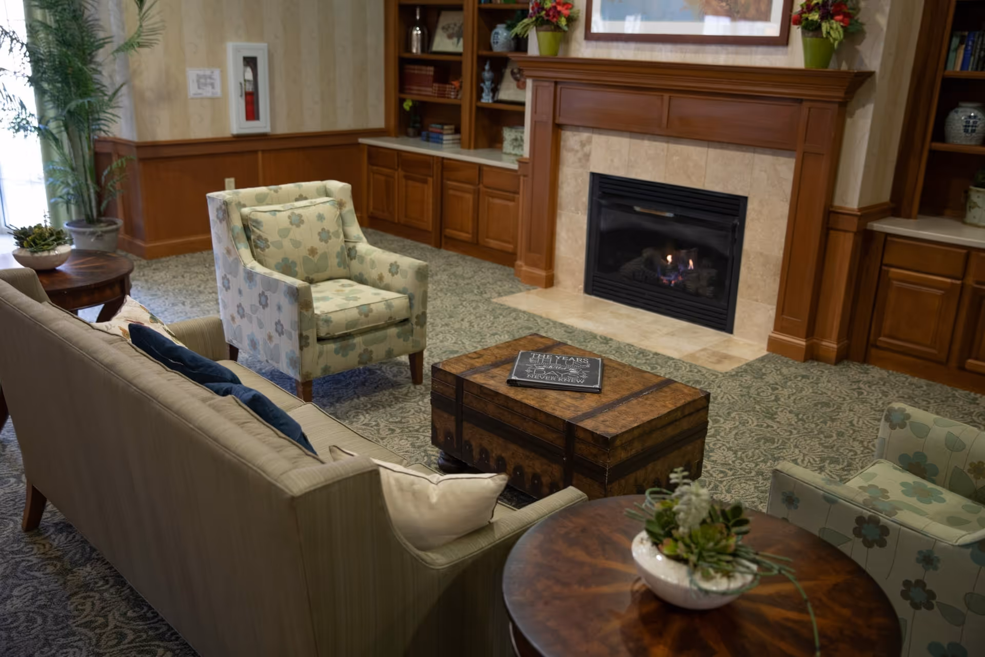 Comfortable sitting area with sofas and armchairs arranged around a wooden coffee table in front of a lit fireplace.