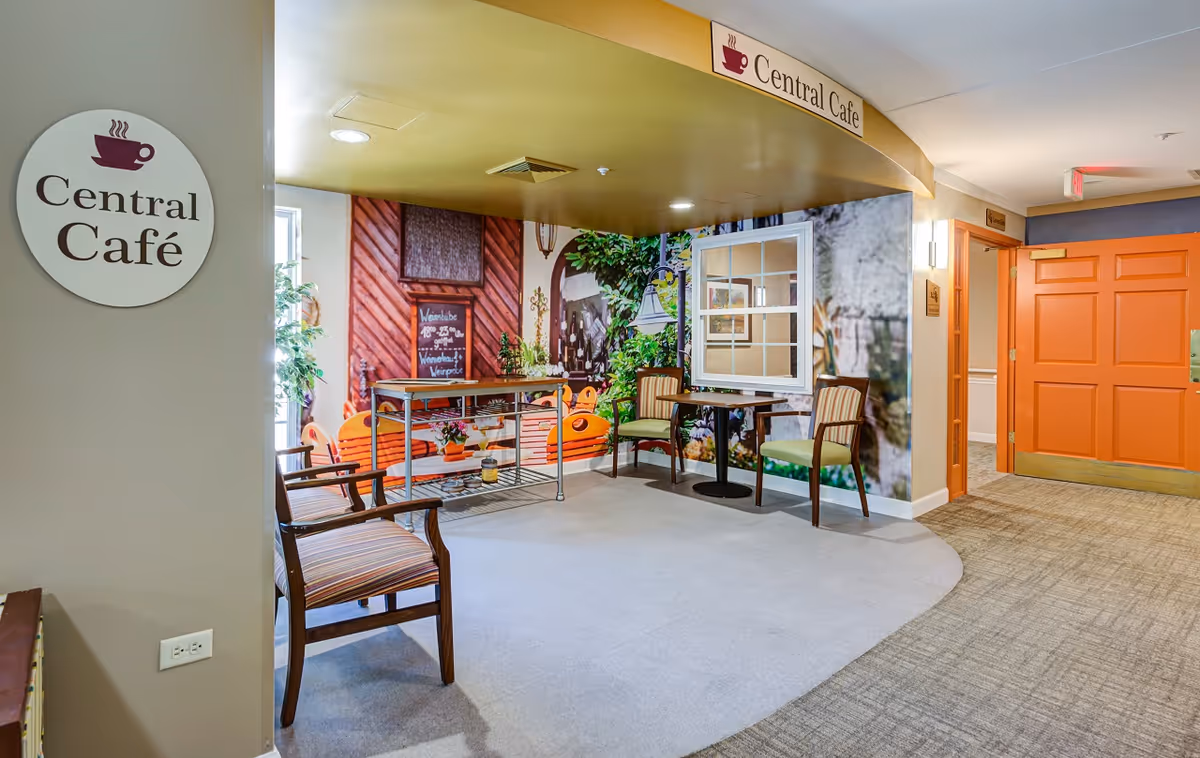 Bright indoor café seating area labeled 'Central Café' with chairs, small tables, a decorative mural wall, and an orange hallway door.