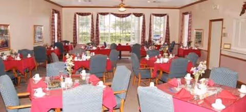 Bright dining room with red tablecloths and neatly set tables in a senior facility.