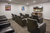 A small media room with two rows of leather recliner chairs facing a wall-mounted television and framed artwork on the walls.
