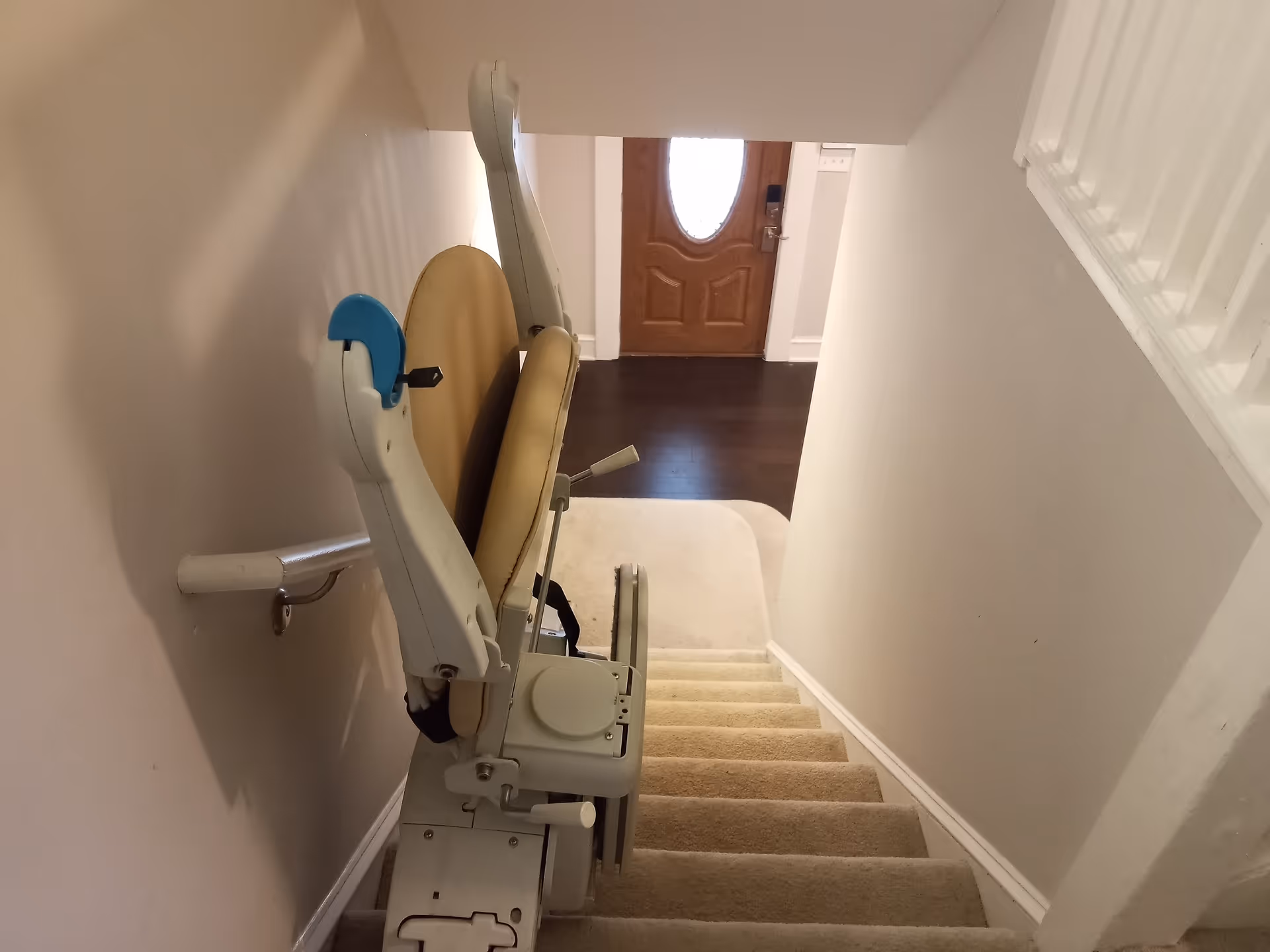 Indoor staircase with a beige chair lift mounted to the wall near a wooden door.
