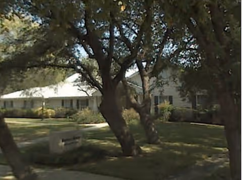 Exterior view of a senior living facility with trees and a green lawn.