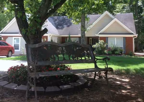 Front view of a single-story senior living facility with a decorative bench under a tree.