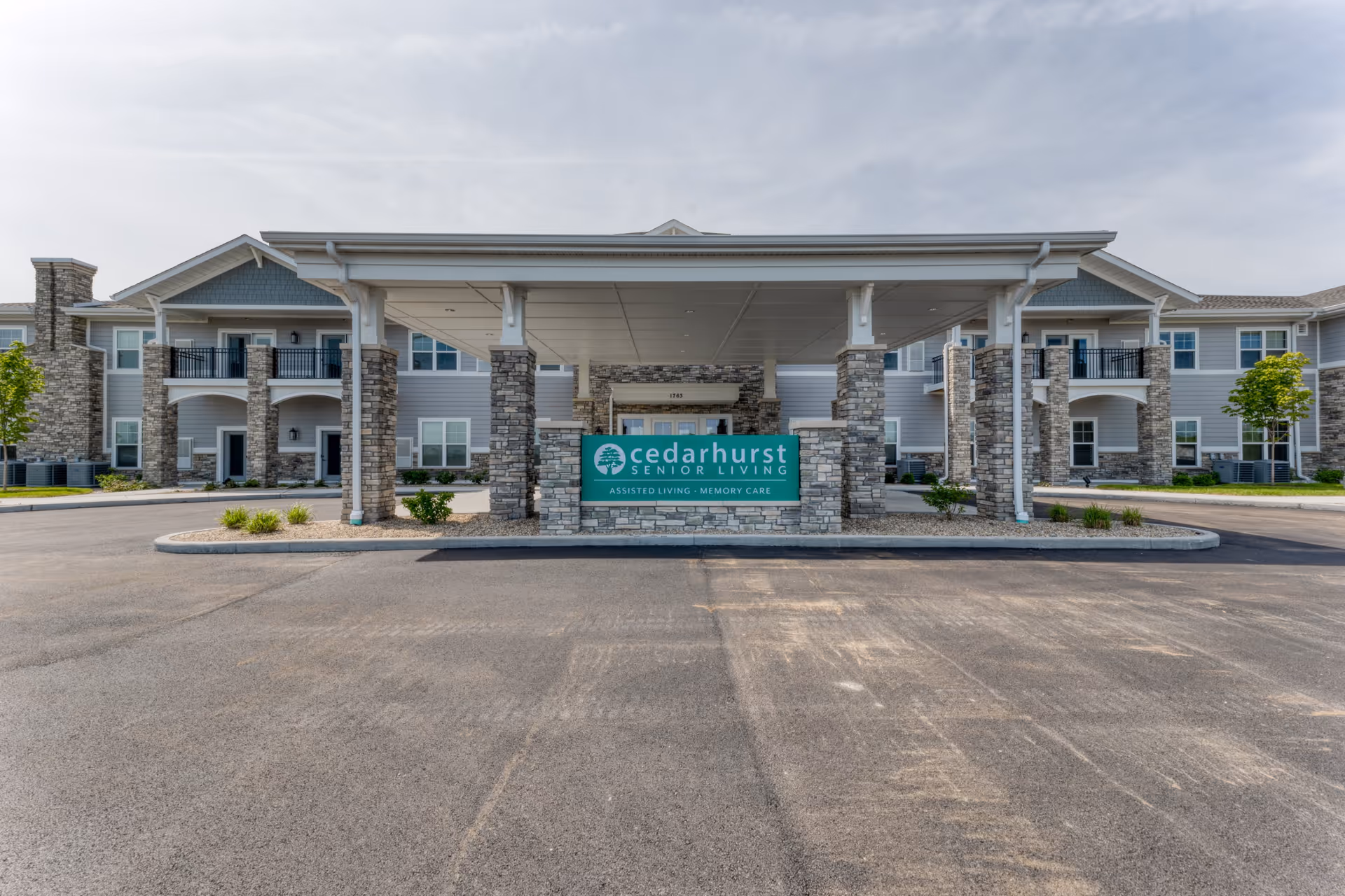 Front exterior view of Cedarhurst Senior Living of Dyer building with a covered entrance supported by stone pillars and a sign displaying the facility name and services.