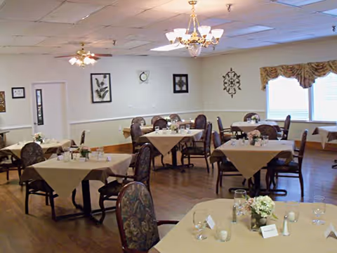 Dining room with multiple tables covered in beige tablecloths and set with place settings under chandeliers.