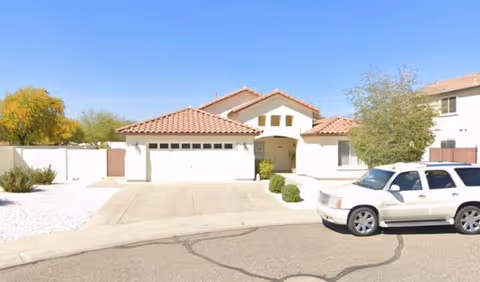 Residential-style, single-story care home with a tiled roof, driveway, and a parked SUV.