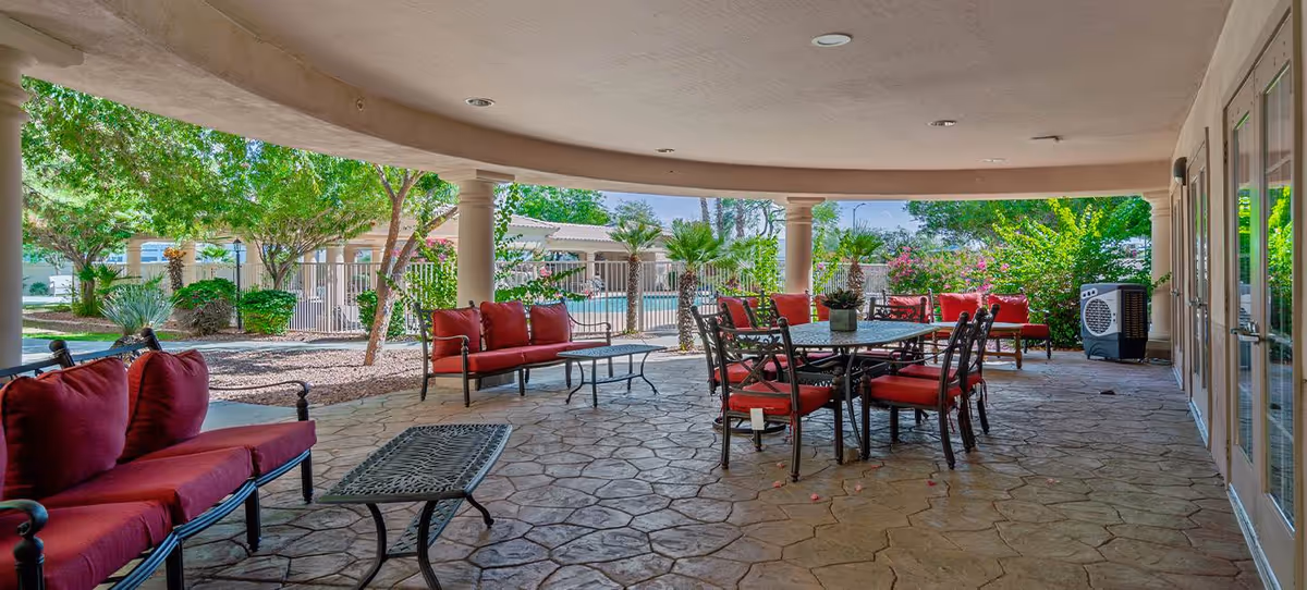 Covered outdoor patio with red-cushioned seating and a dining table overlooking a fenced pool and landscaped grounds.