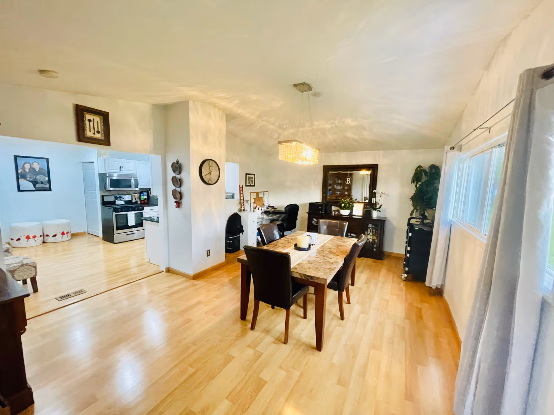 Bright open dining room with a wooden table and chairs, a chandelier, sideboard and a view into the adjacent kitchen.
