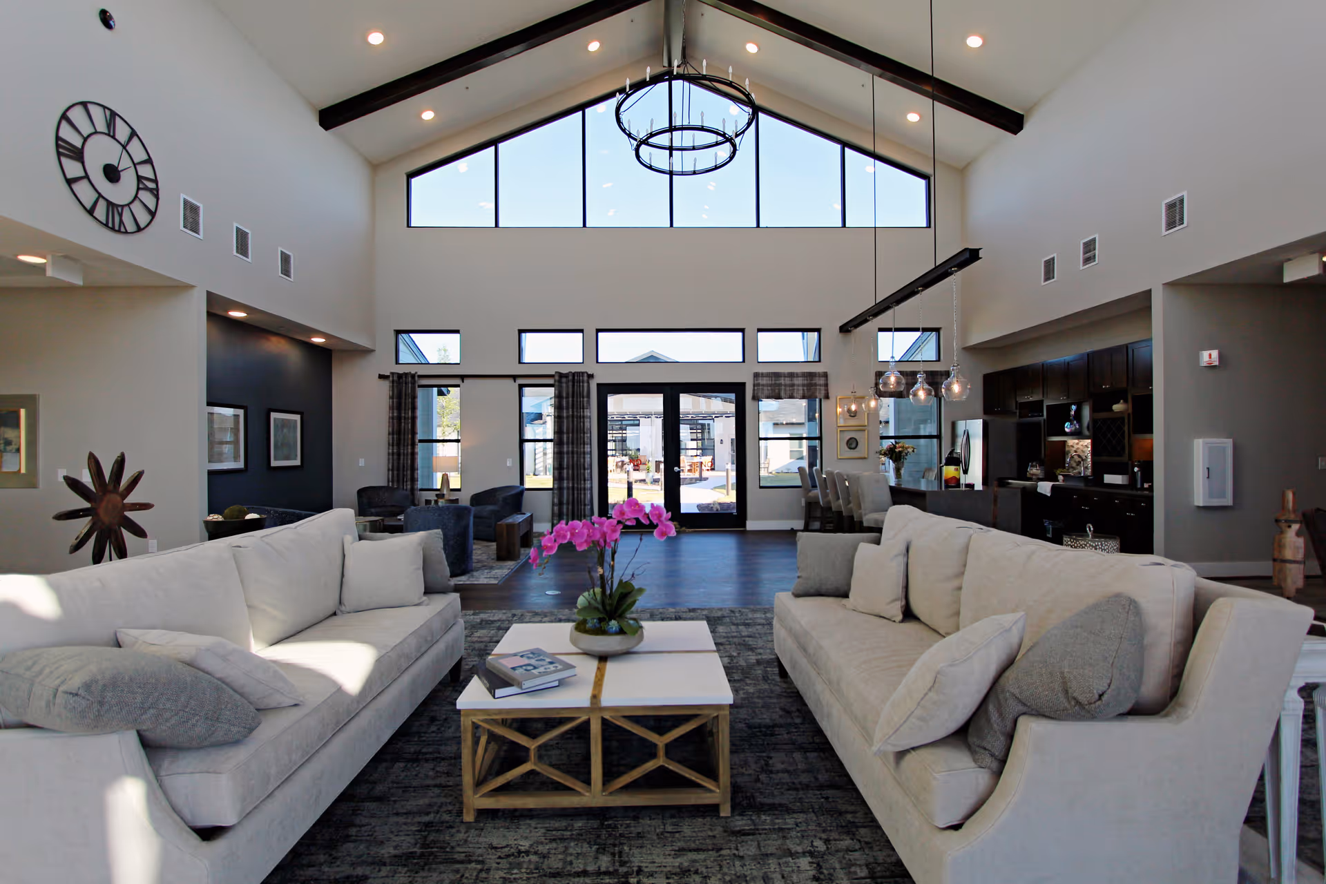 Bright, spacious living room with two light-colored sofas facing a central coffee table, high vaulted windows, and a chandelier.