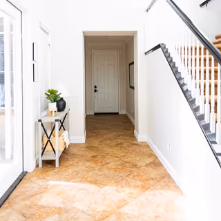 Bright entry hallway with a small console table, tiled floor, staircase on the right, and a door at the far end.