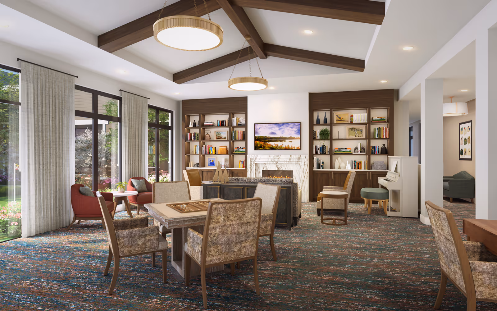 Bright communal lounge with seating, game tables, a fireplace, built-in bookshelves and large windows overlooking a garden.