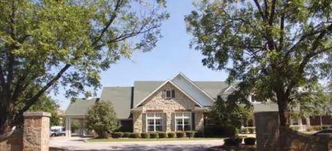 Front view of a brick-and-stone senior living building surrounded by trees.