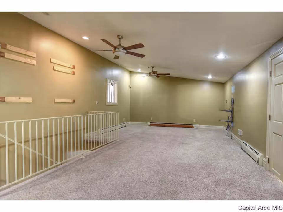 Spacious carpeted loft/living area with ceiling fans, recessed lights, a railing overlooking stairs, and neutral-colored walls.