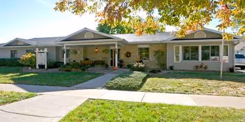 Single-story senior living home with a front porch, shrubs, and a walkway to entrances.