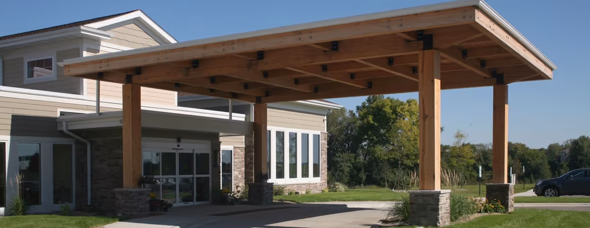 A modern senior living facility entrance with a large wooden porte-cochère and glass doors.