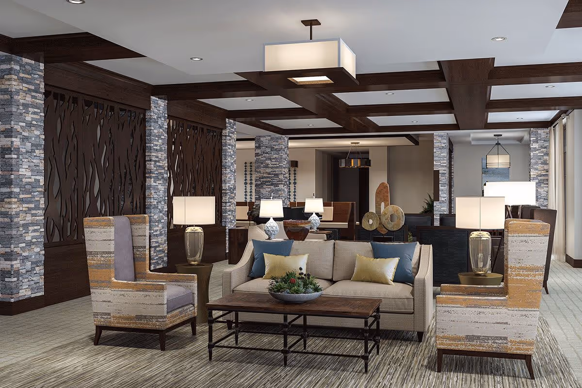 A modern and spacious living room area with a beige sofa adorned with blue and yellow pillows, two patterned armchairs, a wooden coffee table with a decorative plant, multiple table lamps, and stone accent columns. The ceiling features dark wooden beams and a large rectangular light fixture.