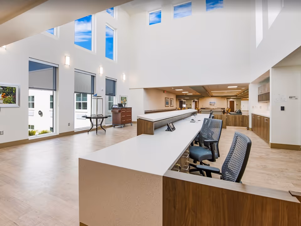 Bright, modern reception/lobby area with a long front desk, office chairs, high windows, and open seating.