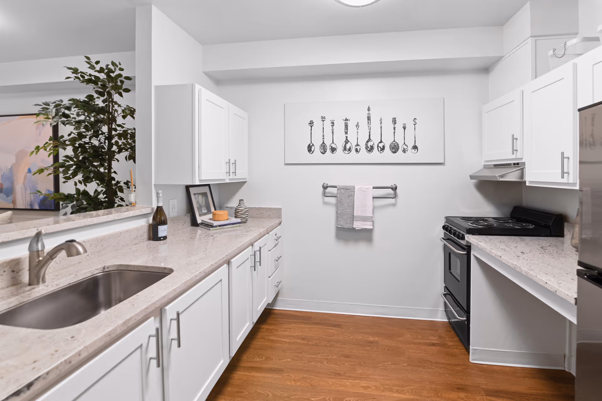 Bright modern kitchen with white cabinets, light stone countertops, stainless sink, stove and refrigerator, and wall art above a towel rack.