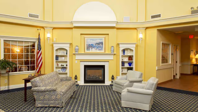 A bright sitting room with a central fireplace flanked by built-in shelves, a sofa, two armchairs, and an American flag.