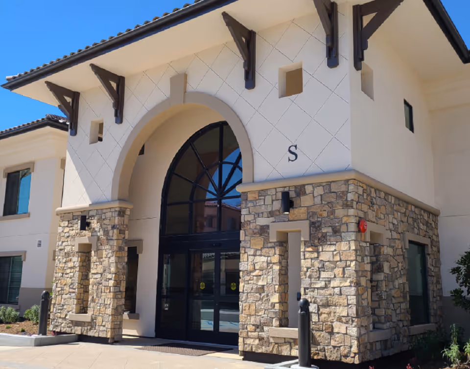 Main entrance of a stone-and-stucco building with a large arched glass doorway and an 'S' on the facade.