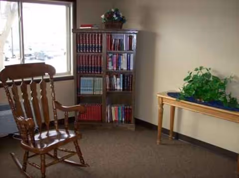 Wooden rocking chair near a bookshelf and a plant table in a cozy indoor living area.