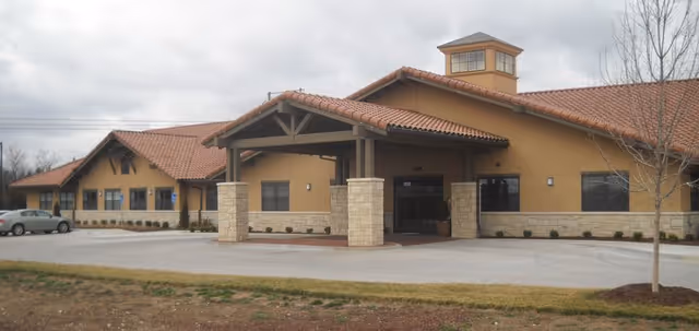 Exterior view of a tan senior living facility with a covered entrance and tile roof.
