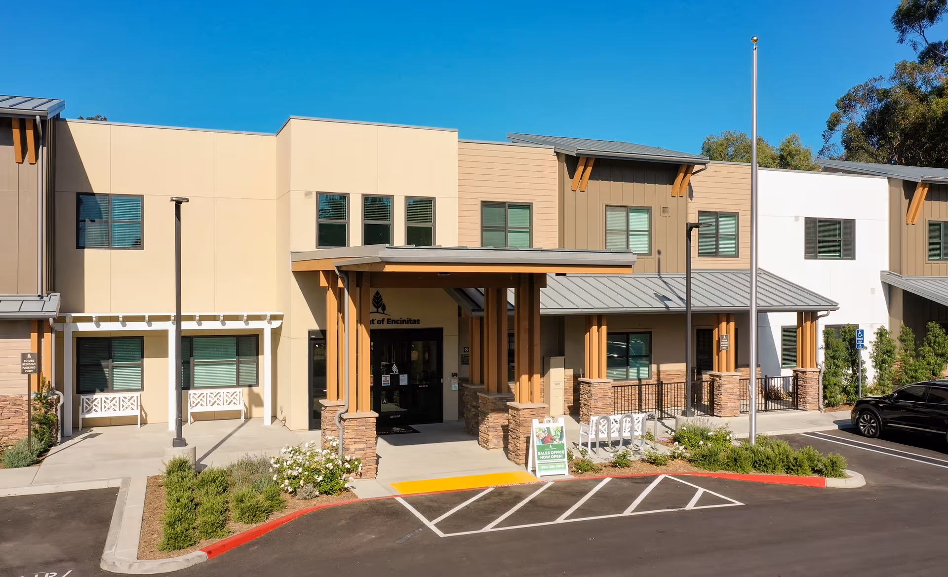 Exterior front view of Westmont of Encinitas senior living facility building with a covered entrance, parking spaces, landscaping, and clear blue sky.