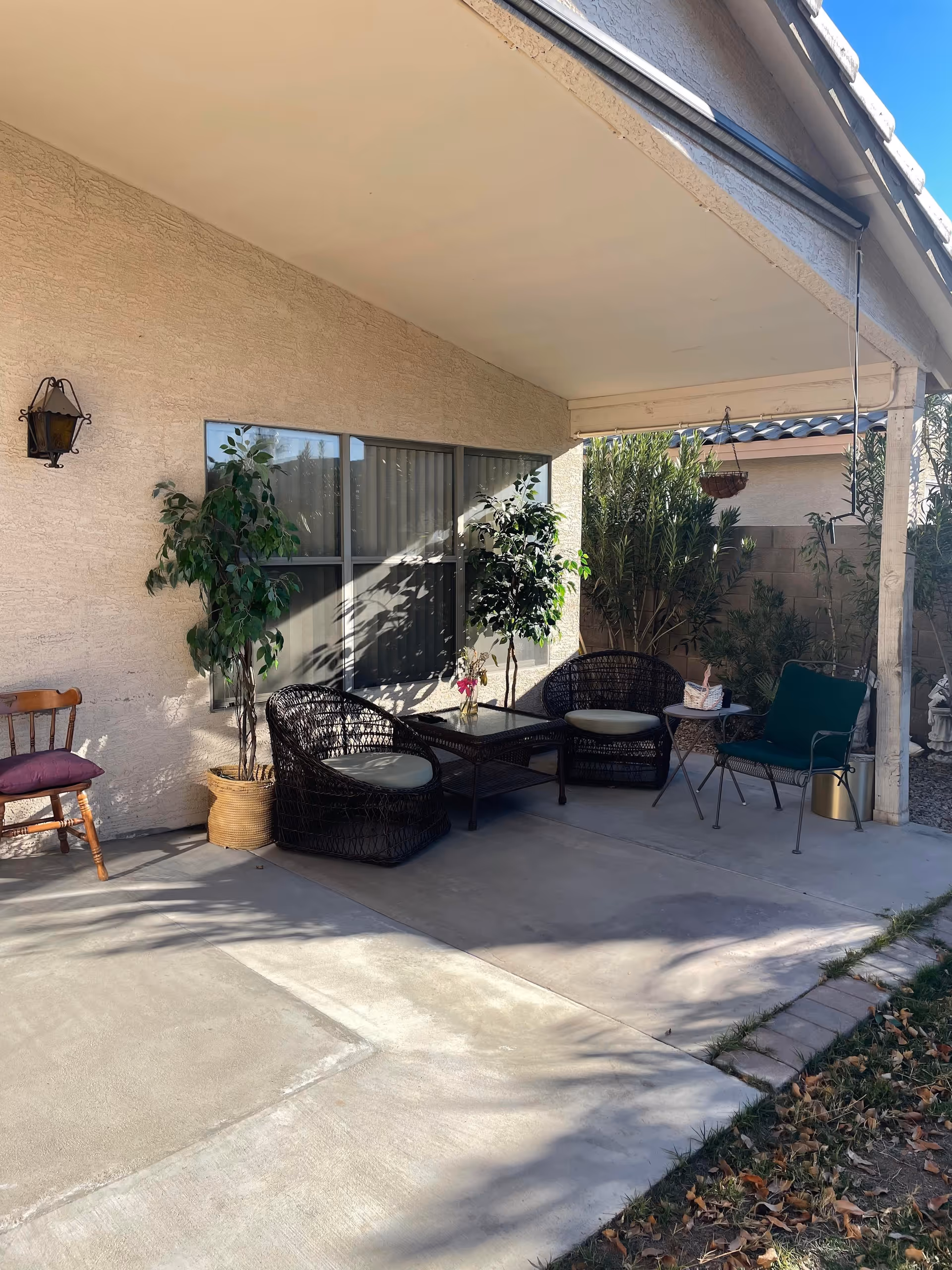 Covered outdoor patio with wicker chairs, a small table, potted plants and extra seating under a porch.
