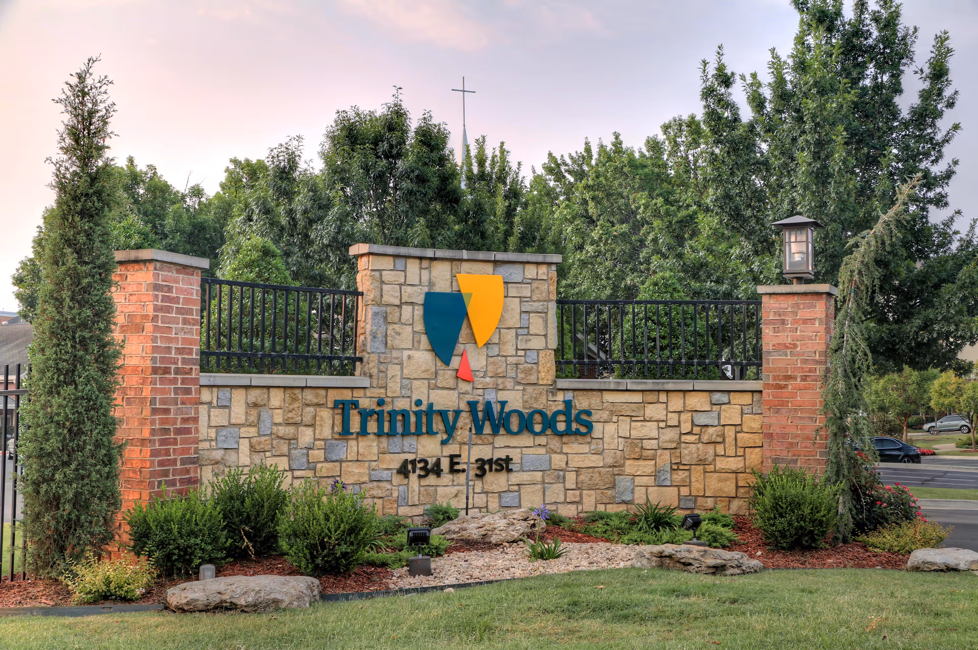 Stone entrance sign reading 'Trinity Woods' set in landscaped grounds with trees behind.