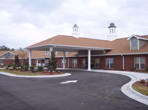 Brick senior living facility with curved driveway and covered entrance under cloudy skies.