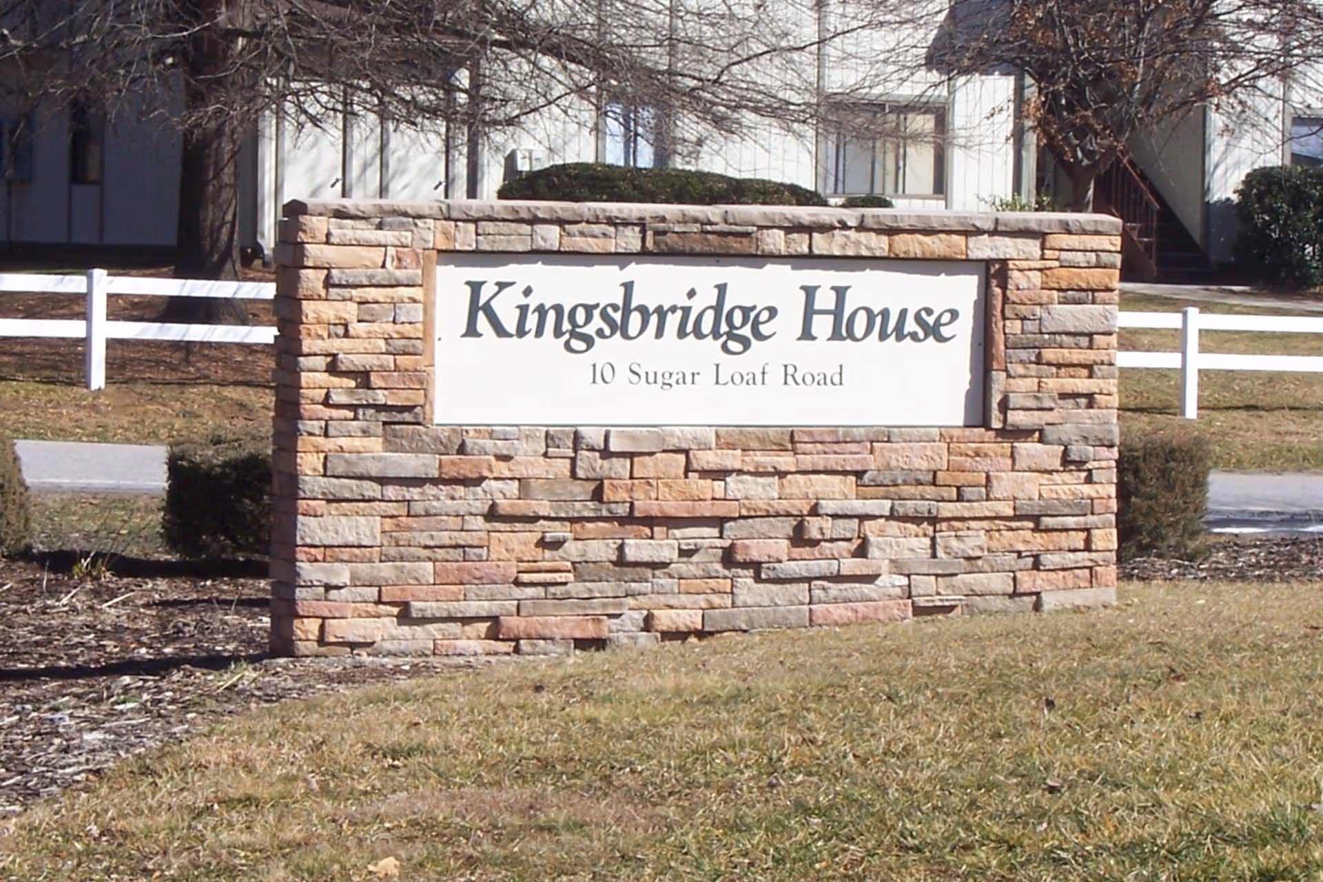 Stone entrance sign on a grassy lawn reading "Kingsbridge House, 10 Sugar Loaf Road" in front of a building.