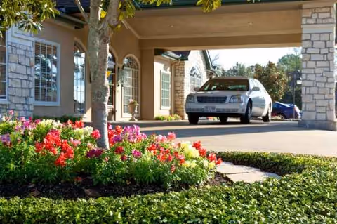 Entrance to Carriage Inn Huntsville with a white car under a covered drop-off, flowering landscaping.