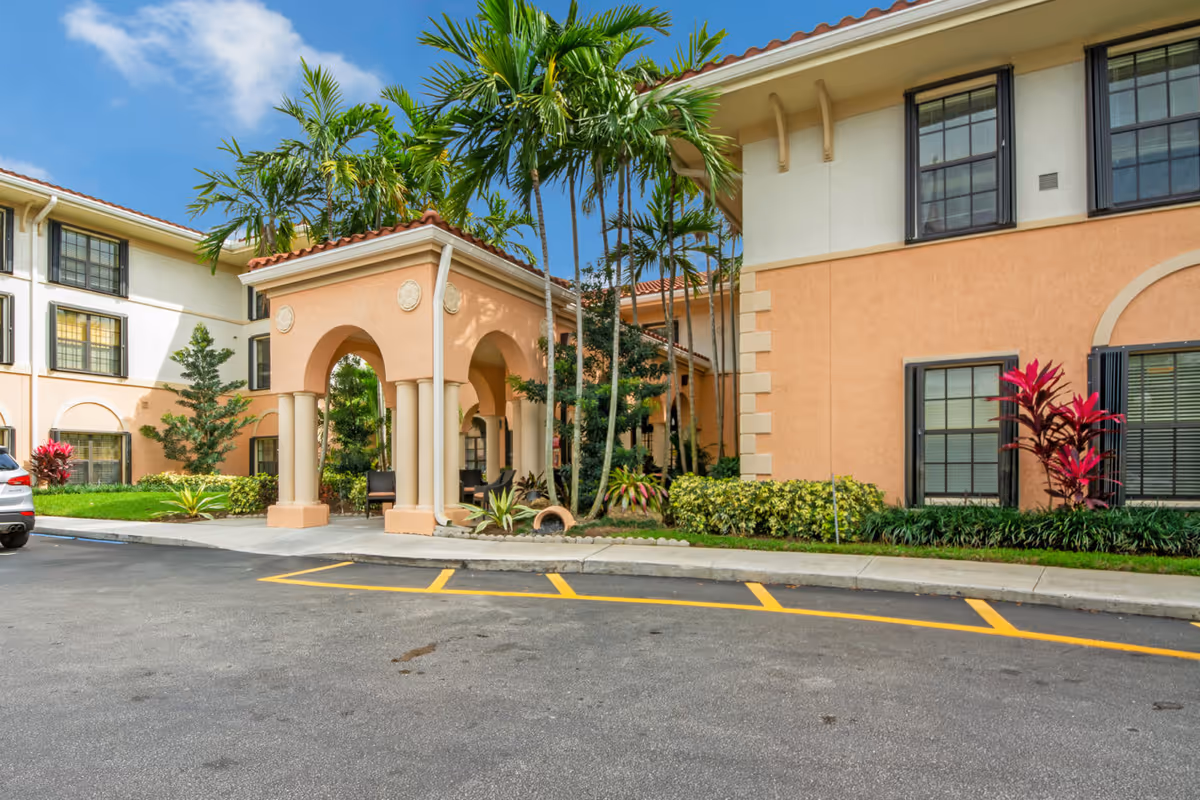 Exterior view of a senior living facility named Presidential Place, featuring a peach-colored building with arched entryways, palm trees, and landscaped greenery under a blue sky.