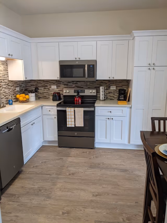Bright modern kitchen with white cabinets, stainless steel appliances, tiled backsplash, and wood-look flooring.