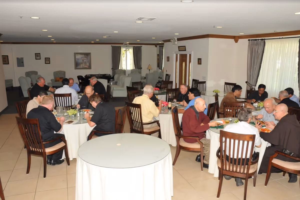 A dining room with round tables where older adults sit together eating and talking.