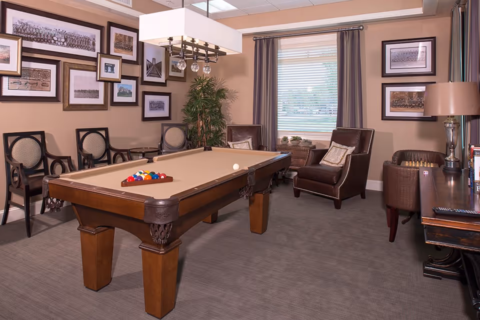 A well-appointed game room with a pool table, framed pictures on the wall, and several chairs and armchairs.