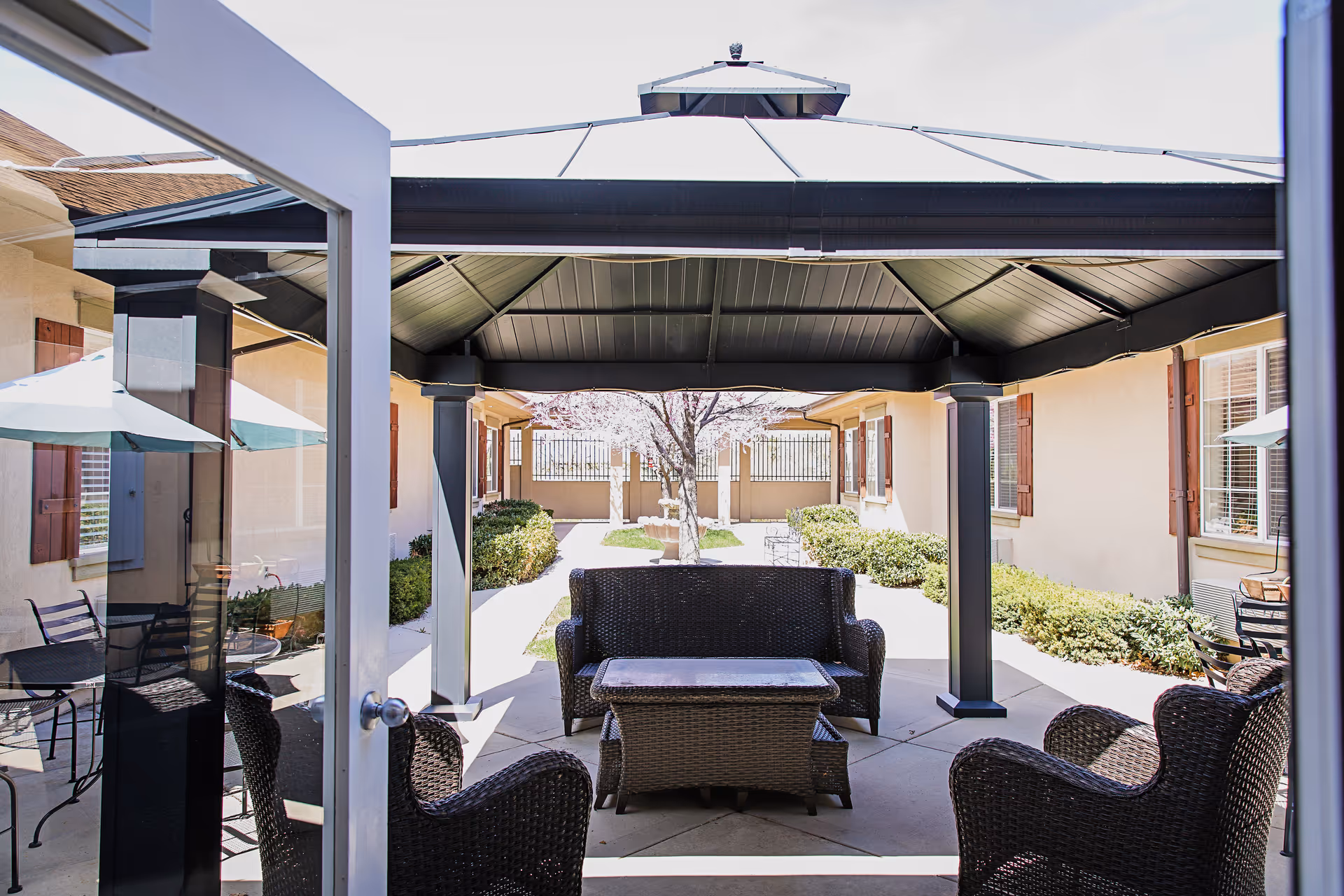 Shaded outdoor courtyard with wicker seating and a central covered gazebo between building wings.