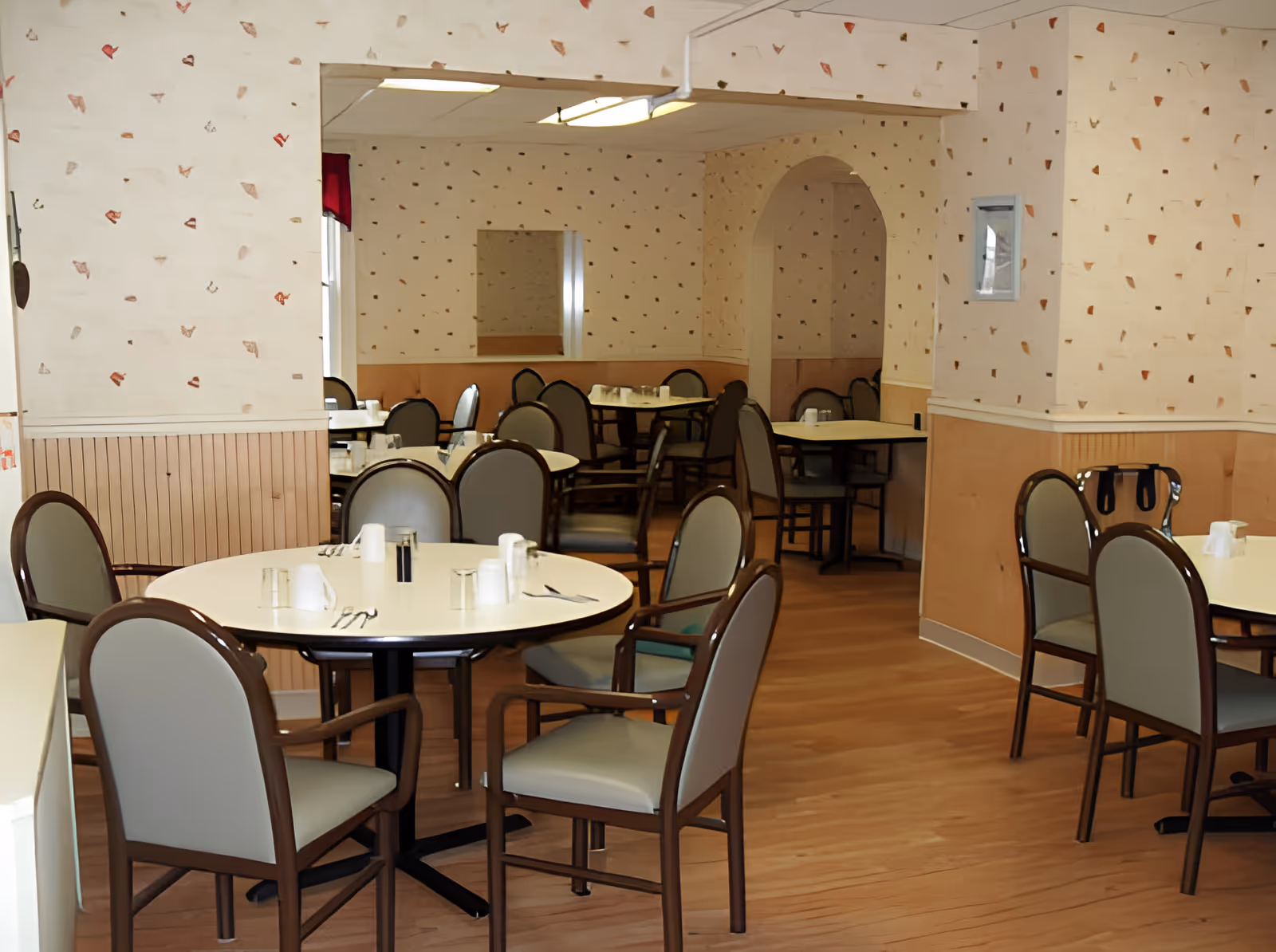 Empty dining room with round tables and chairs set for meals inside a senior living facility.