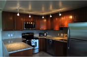 Modern kitchen with dark wooden cabinets, granite countertops, stainless steel appliances including a refrigerator, oven, microwave, and dishwasher. The kitchen has recessed lighting and a small peninsula counter.