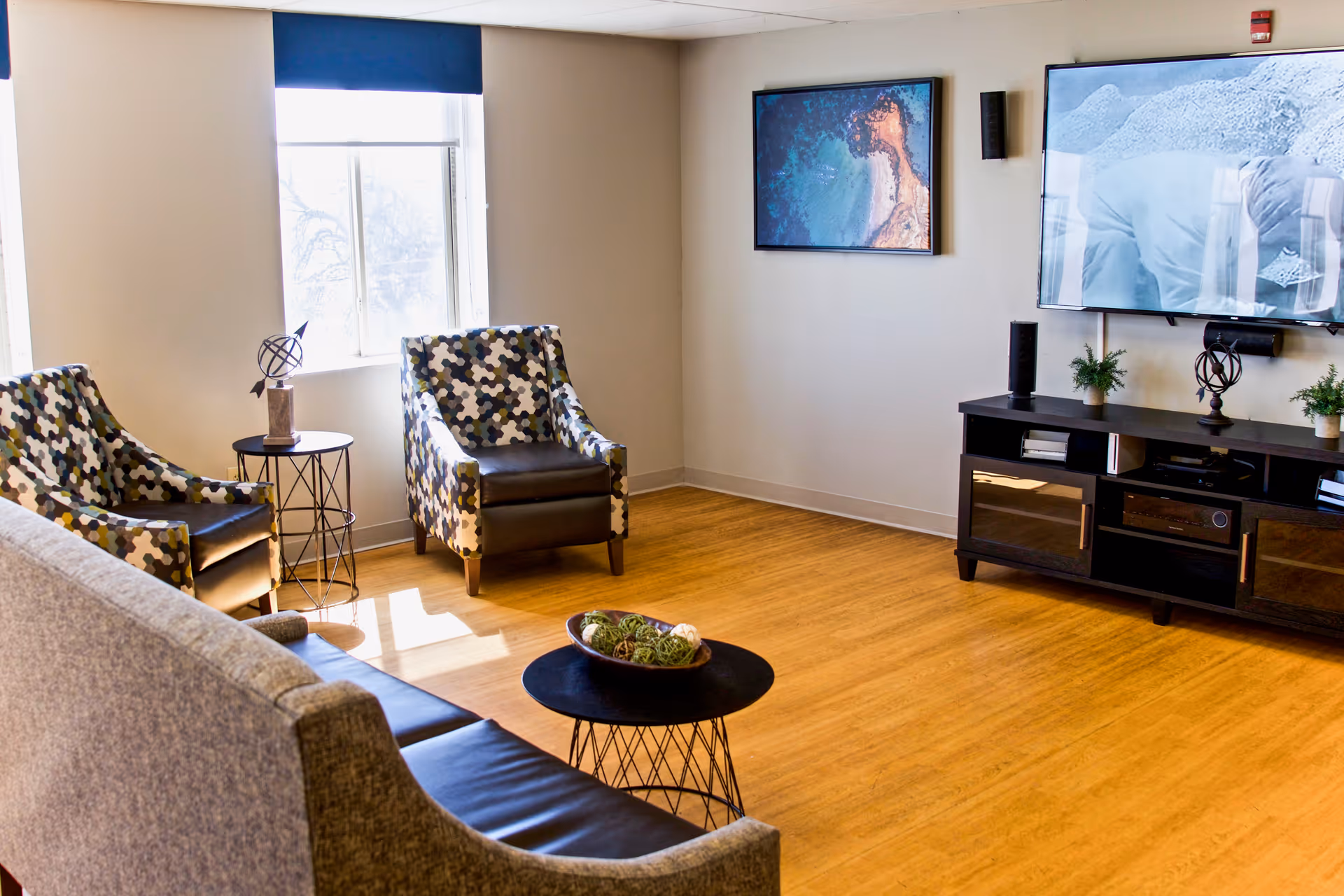 Bright lounge with patterned armchairs, a sofa, a round coffee table, and a wall-mounted TV above a media console.