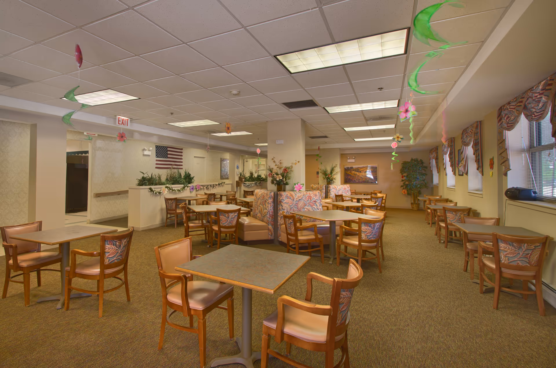 Dining room with multiple tables and chairs, booths, hanging ceiling decorations, and an American flag on the far wall.