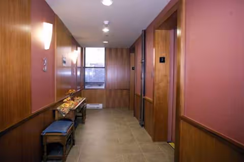 Interior hallway with pink walls, wood paneling, doors, and a bench along the corridor.