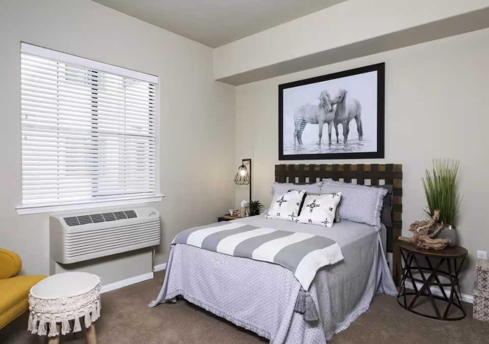 Neatly furnished bedroom with a made bed under framed horse artwork, a window with blinds, bedside tables and decorative accents.